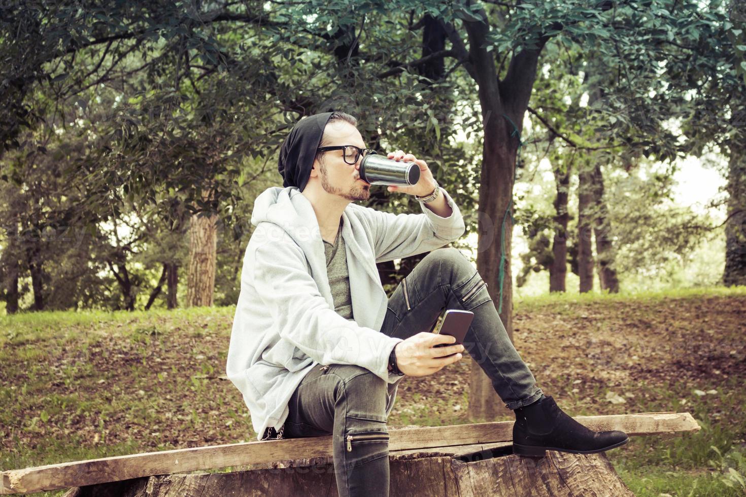 Man using mobile phone while drinking takeaway coffee in the park. photo