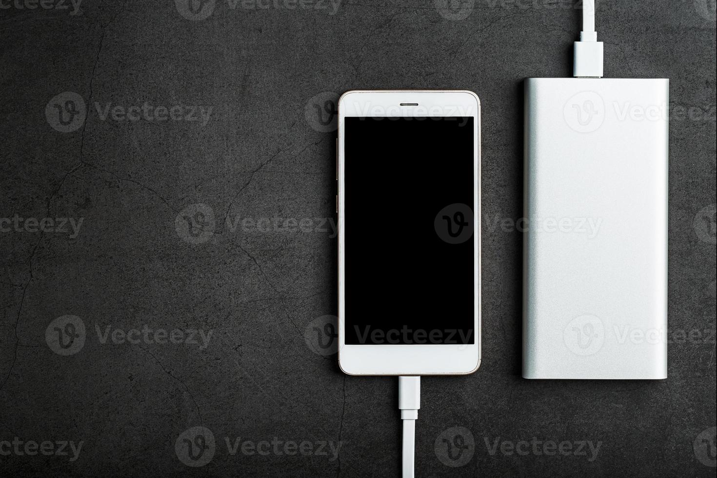 White Smartphone is being charged from the Power Bank on a black background. Top view, free space photo