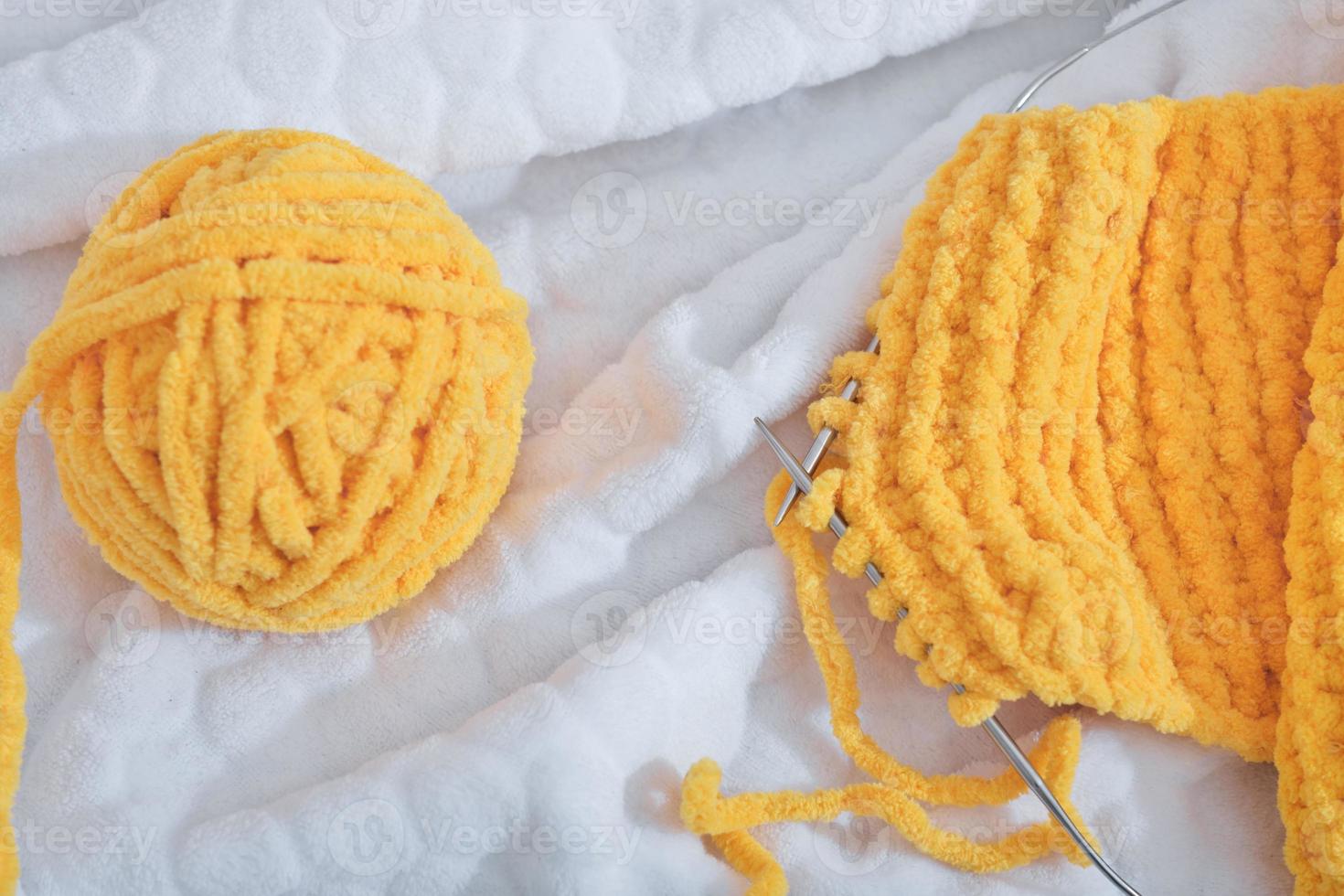 a ball of yellow yarn and needles with knitting scarf on a bed. hobby and leisure, fine motor skills and attention development photo