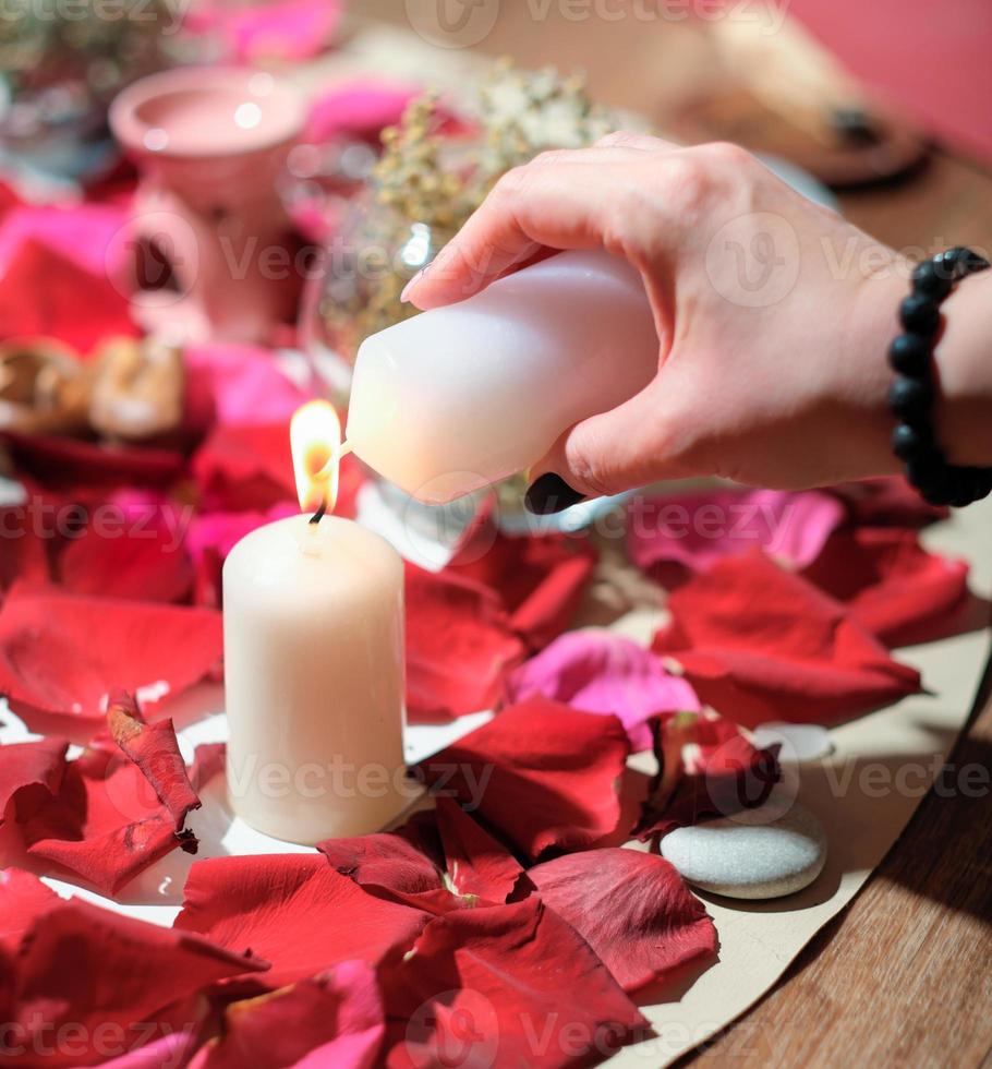 mujer encendiendo una vela sobre fondo de pétalos de rosa. piedras, hierbas y velas durante la práctica espiritual. sesión de rituales mágicos, espiritistas y canalizaciones foto