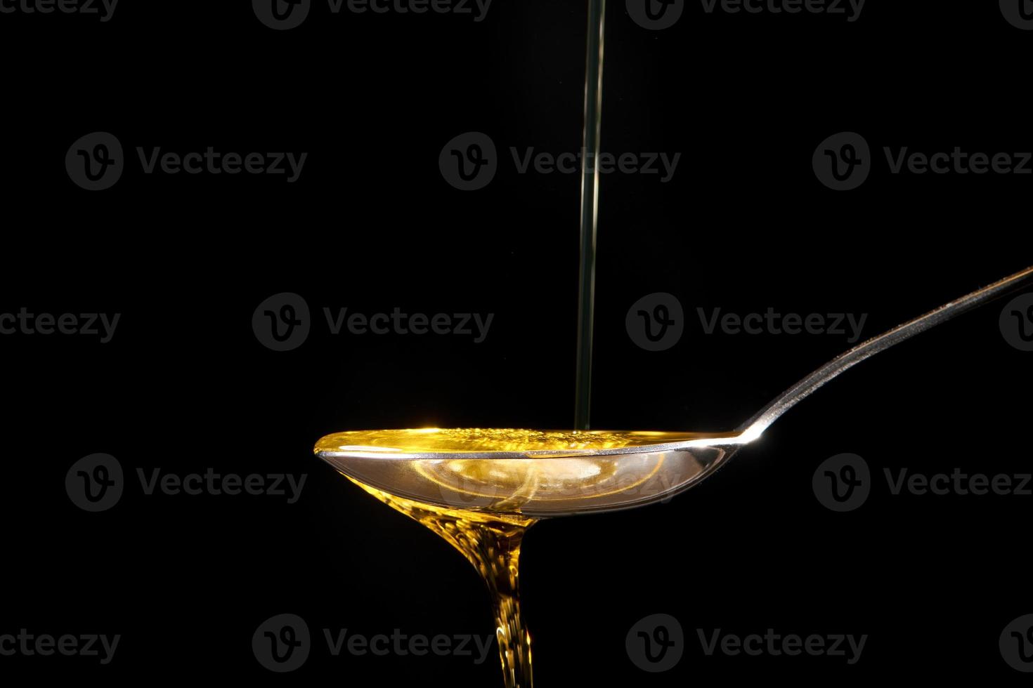 Olive oil is poured from a spoon into a bowl. photo on a black background