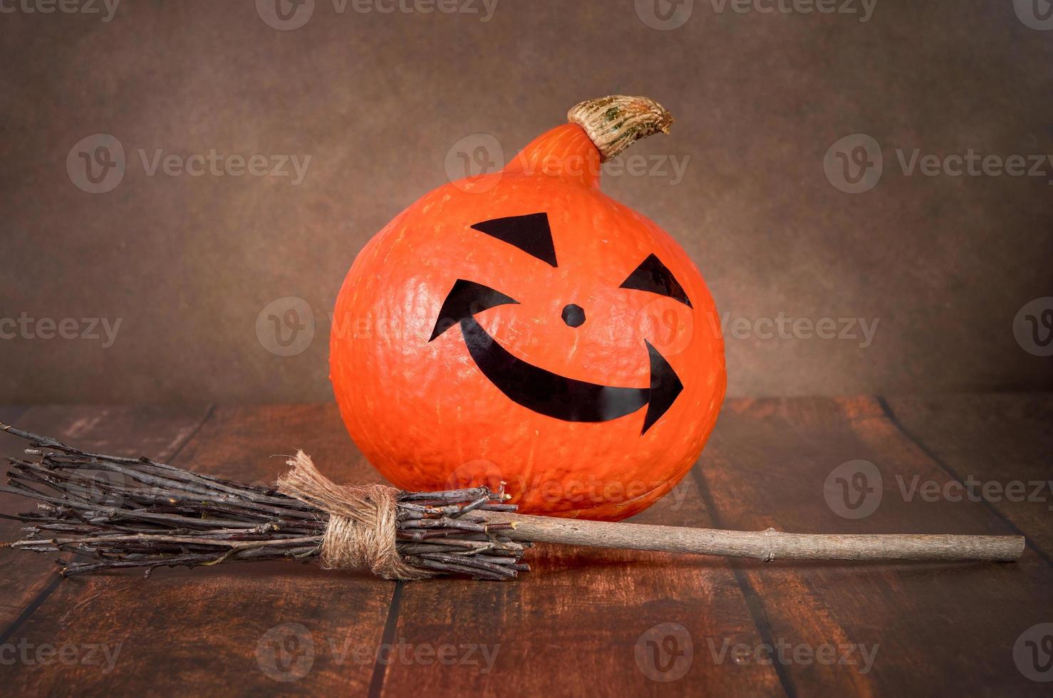 One Halloween pumpkin and a witch's broom on a brown background. photo