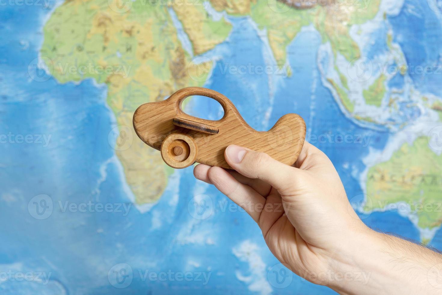 A man's hand holds a wooden toy model of an airplane against the background of a world map. The concept of travel and vacation. photo