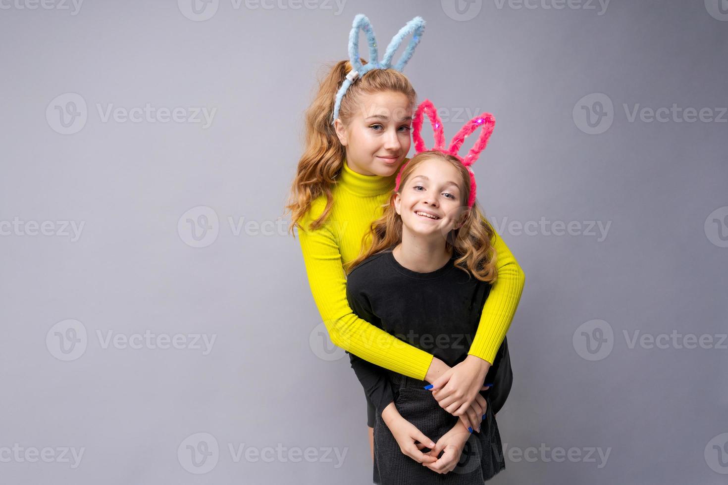 Close-up portrait two cheerful pretty young girls with bunny ears in yellow photo