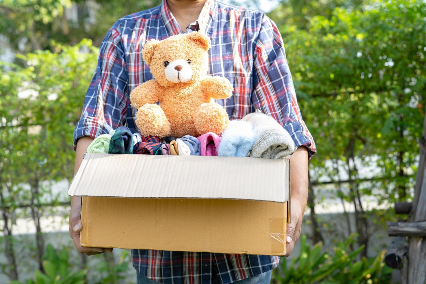 Holding clothing donation box with used clothes and doll at home to support help for poor people in the world. photo