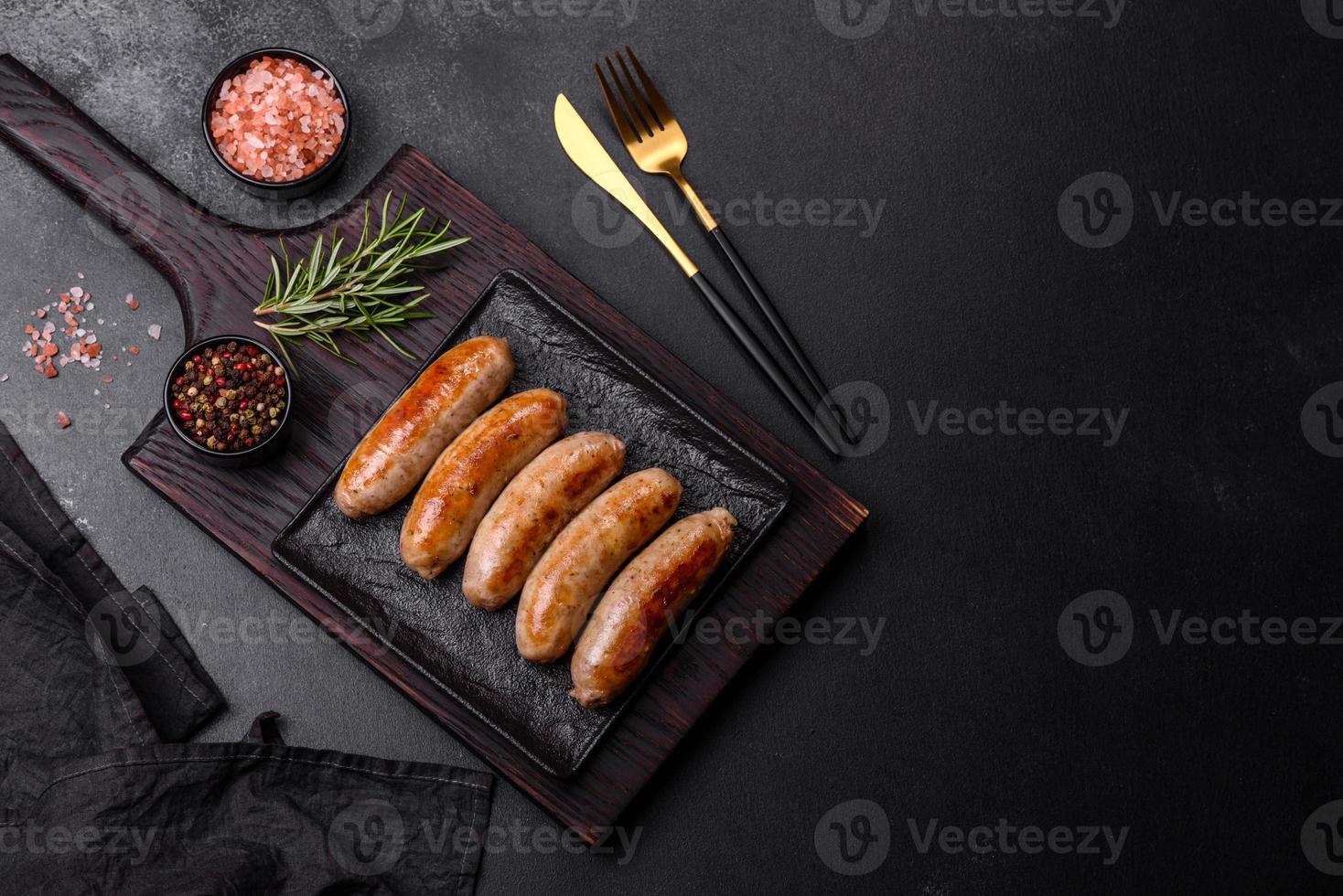 Tasty grilled sausages with spices and herbs on a black slate plate photo