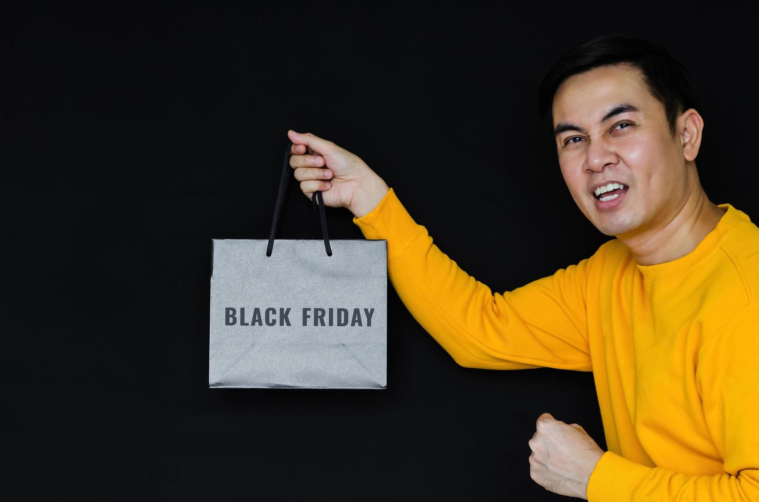Asian happy male holding shopping bag on dark background for Black Friday concept. photo