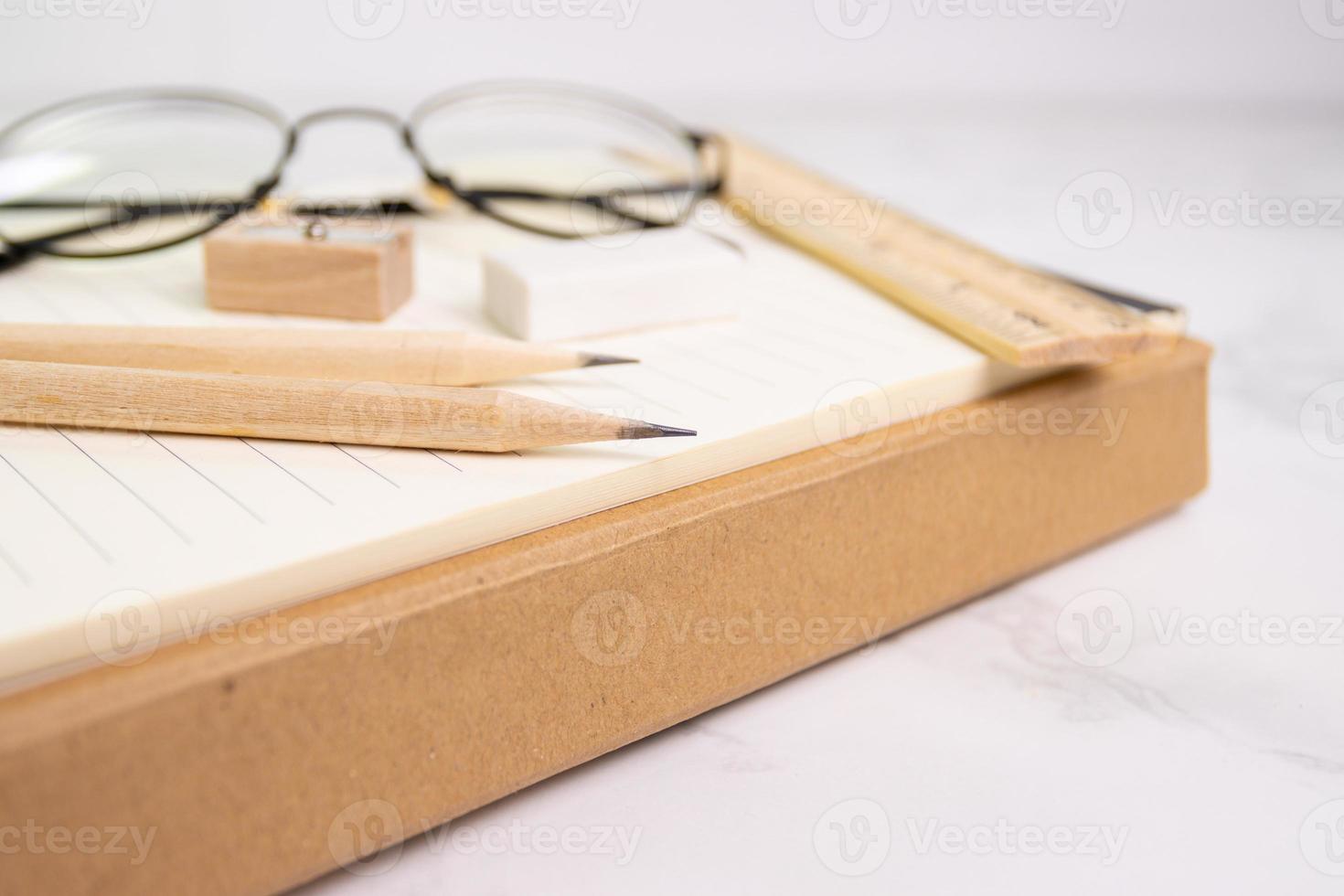 close up a pencil with pencil sharpener on paper and eraser rule, glasses on background photo