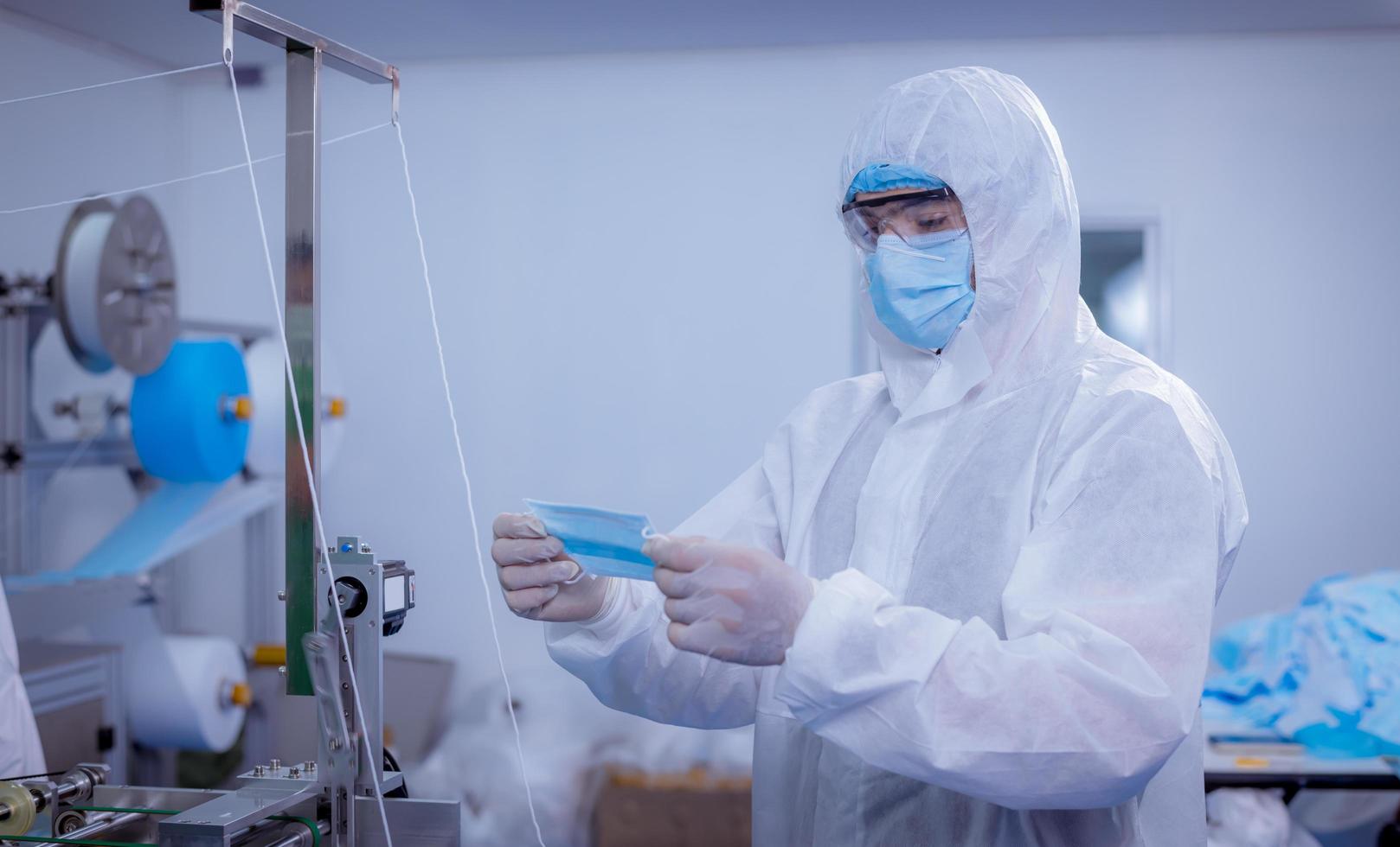 Technician worker wearing protective suite , glove are inspect ion with check  face mask manufacturing process to safe and against from virus. photo