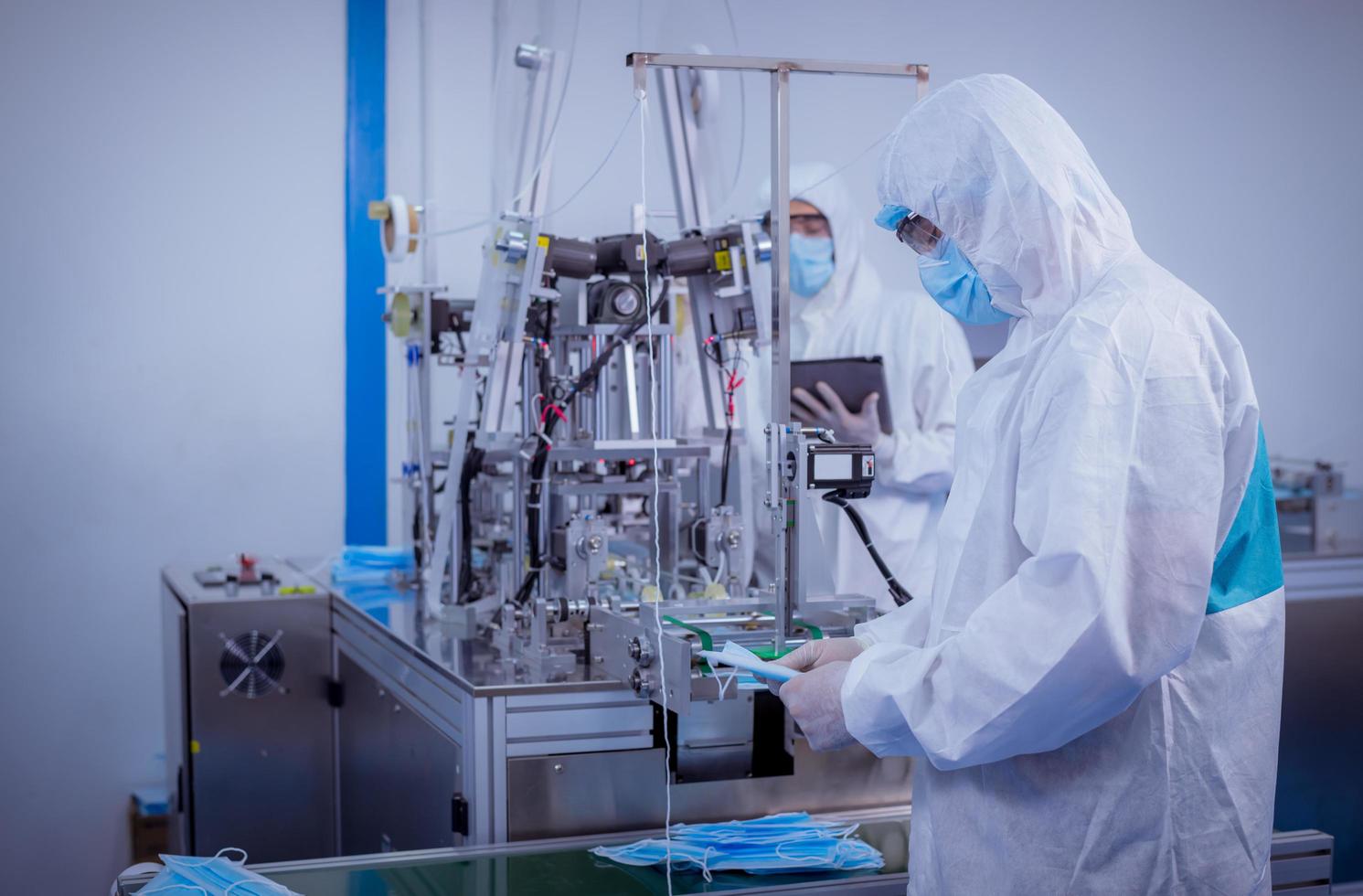 trabajador técnico que usa una suite protectora, los guantes se inspeccionan con el proceso de fabricación de máscaras faciales para asegurarse y evitar el virus. foto