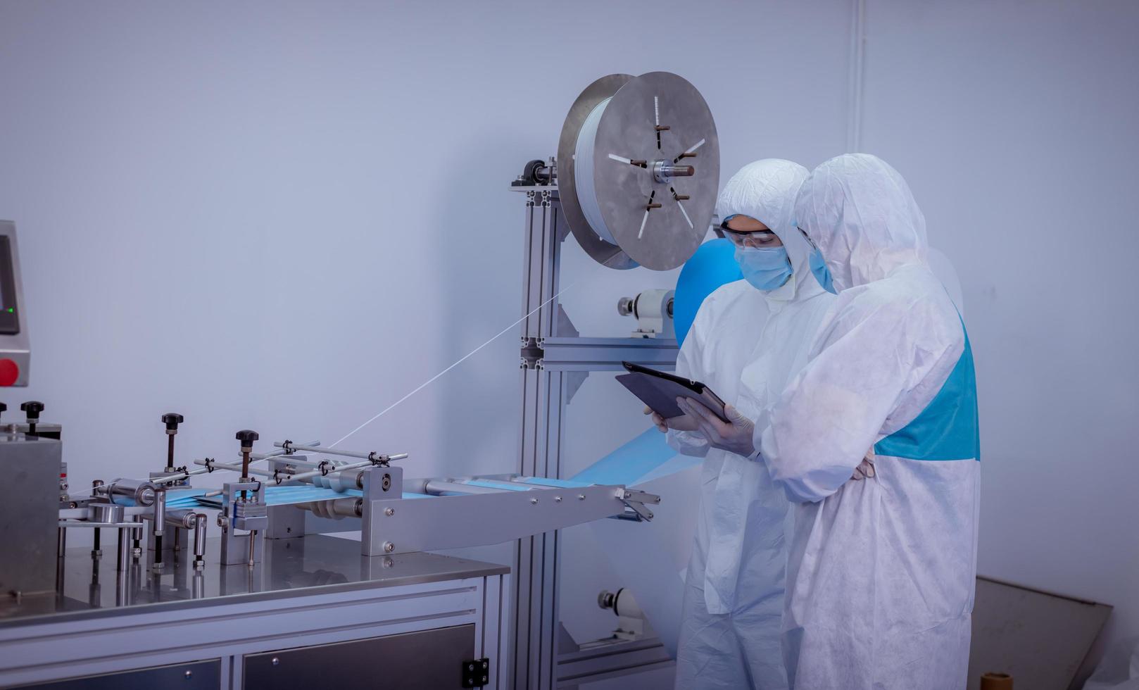 Technician worker wearing protective suite , glove are inspect ion with check  face mask manufacturing process to safe and against from virus. photo