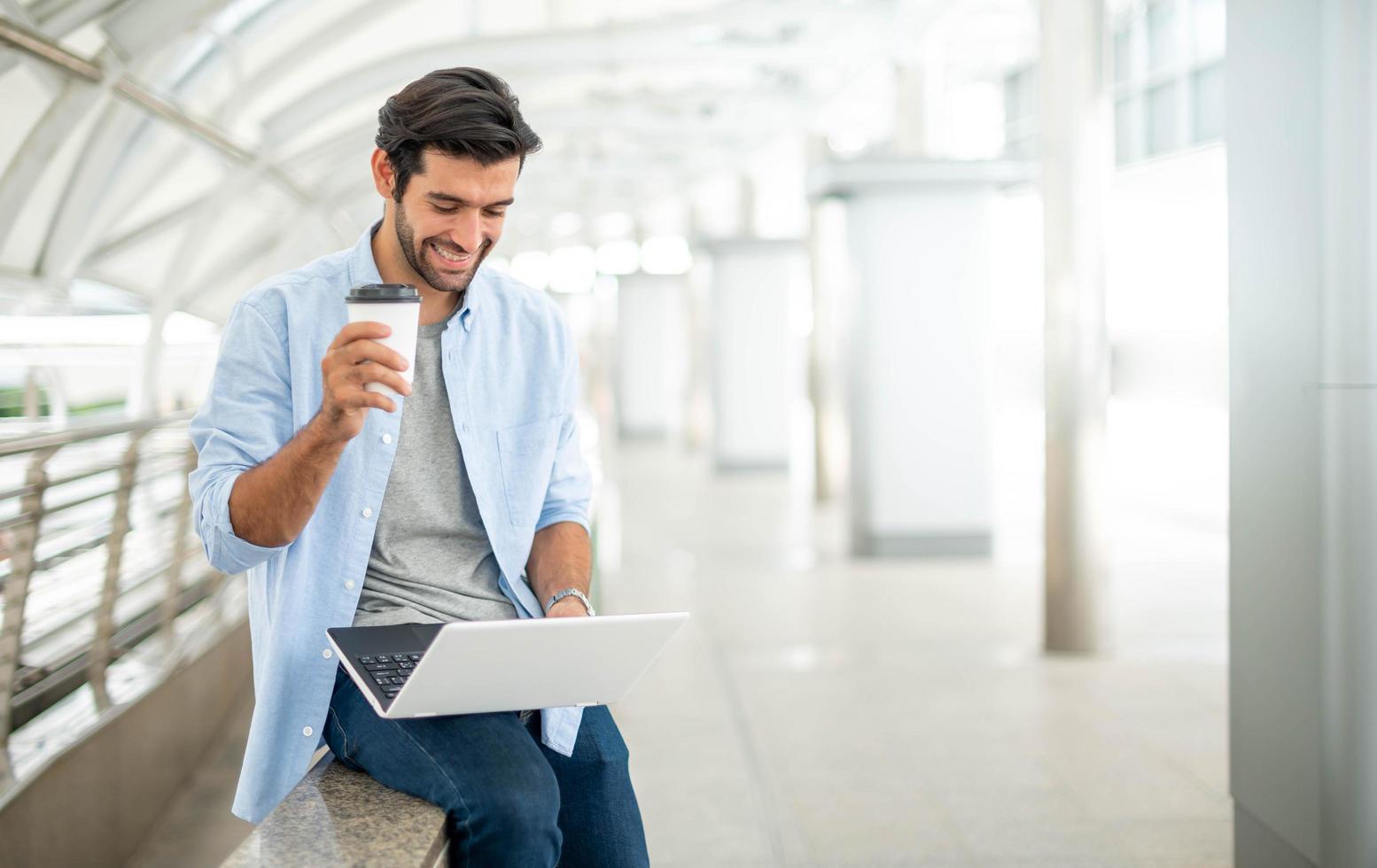 Young caucasian man holding cup of coffee and working on freelance project using portable computer at outer office. photo