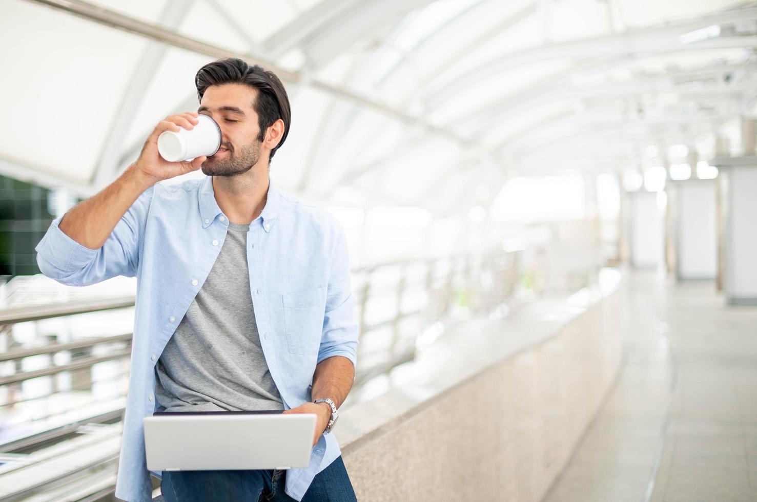 Young caucasian man holding cup of coffee and working on freelance project using portable computer at outer office. photo
