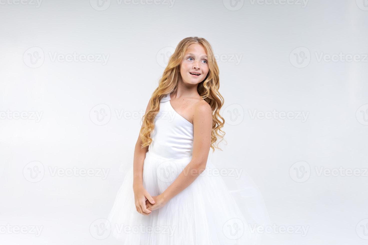 Beautiful cute girl in white dress with long wavy hair posing in studio photo