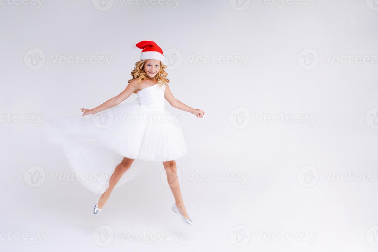 Joyful pretty girl in Red Santa Claus Hat and white dress Laughs and jumps photo