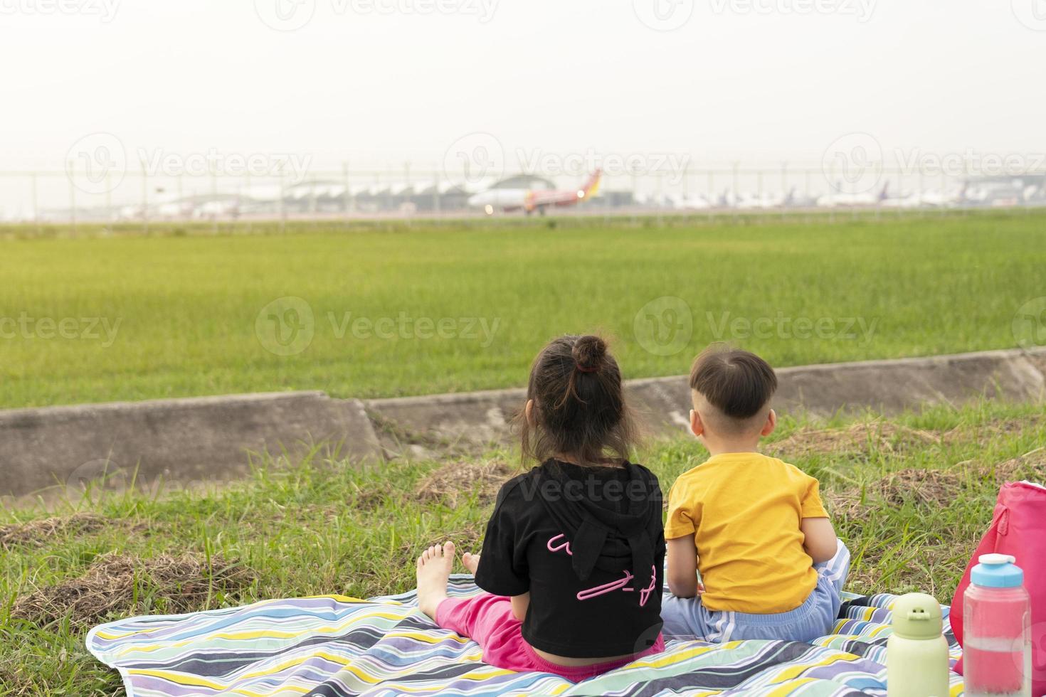 Happy children sit and watch planes take off and land beside the airport. Children dream to fly and become a pilot. photo