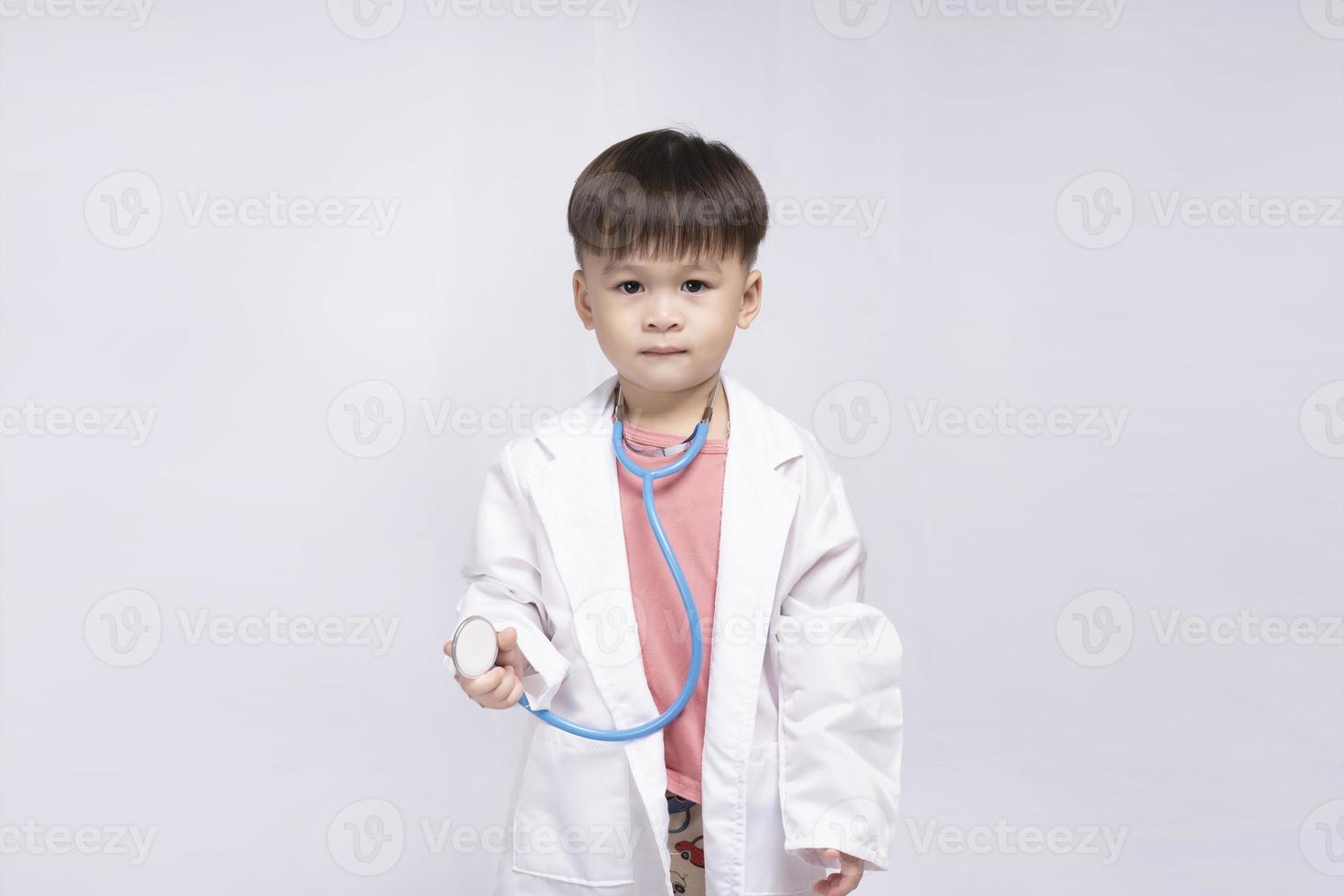 Young cute Asian boy wearing a medical uniform holding a stethoscope playing happy doctor on white background. Preschool children pretend to be a pediatrician. photo