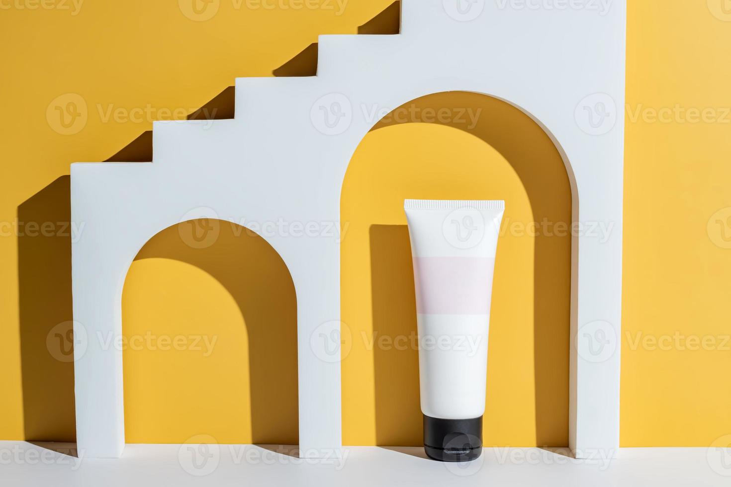 Beauty product concept. White tube of cream on yellow background. Front view. Trendy showcase with hard light. Unbranded package. photo