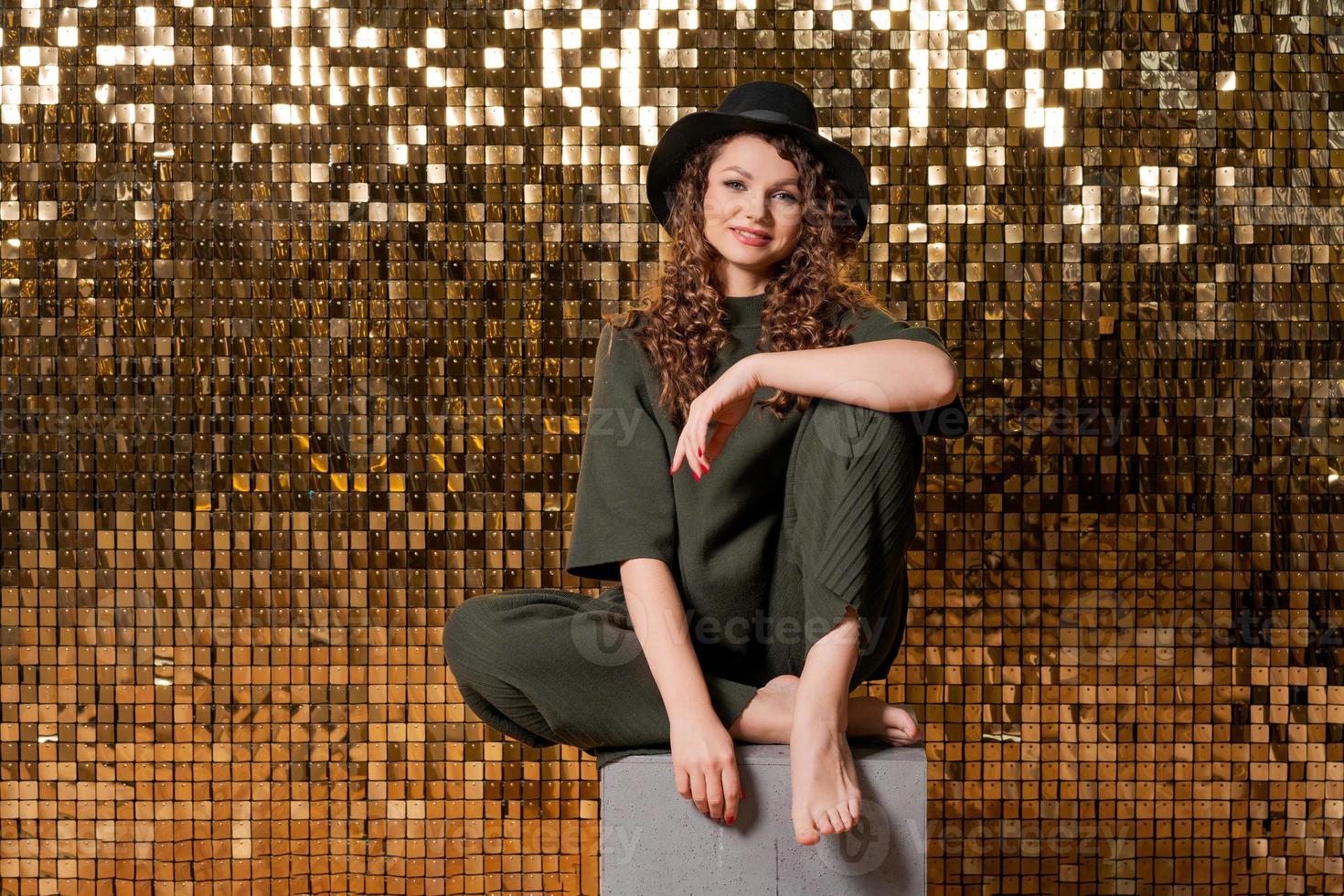 Happy beautiful girl in black hat in studio against background shiny golden photo