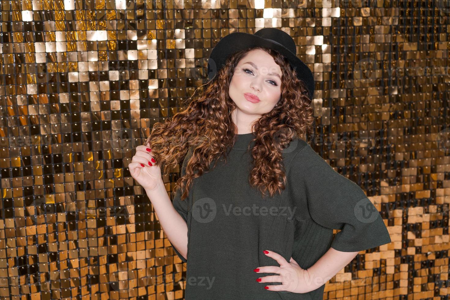 Festive mood in beautiful young woman on background shiny golden wall, smiles photo