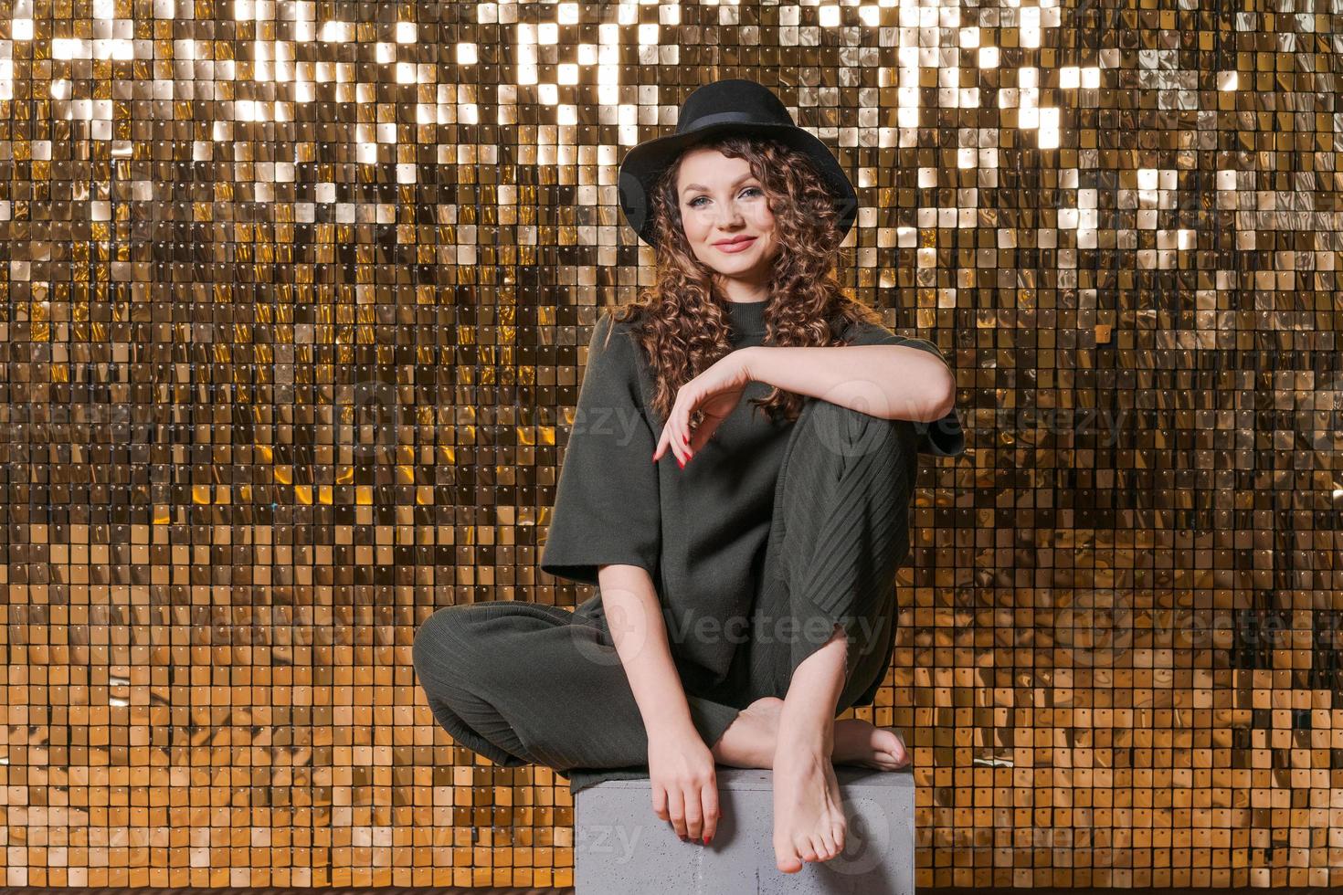 Festive mood in beautiful young woman on background shiny golden wall, smiles photo