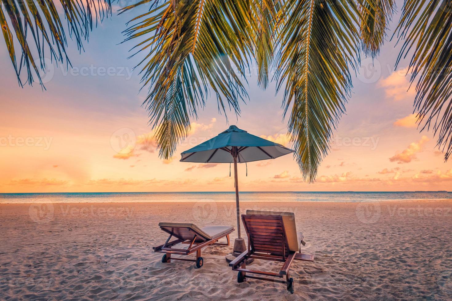 Beautiful tropical sunset scenery, couple chairs, loungers, umbrella under palm tree. Closeup sea sand sky horizon, colorful twilight clouds, relax tranquil vacation landscape. Summer holiday, idyllic photo