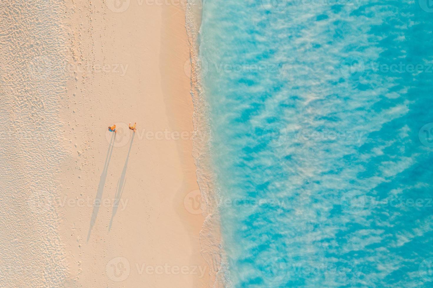 Aerial view of couple walking on beach with sunlight close to turquoise sea waves. Top view of summer beach landscape, romantic inspirational couple vacation, romance holiday. Freedom travel template photo