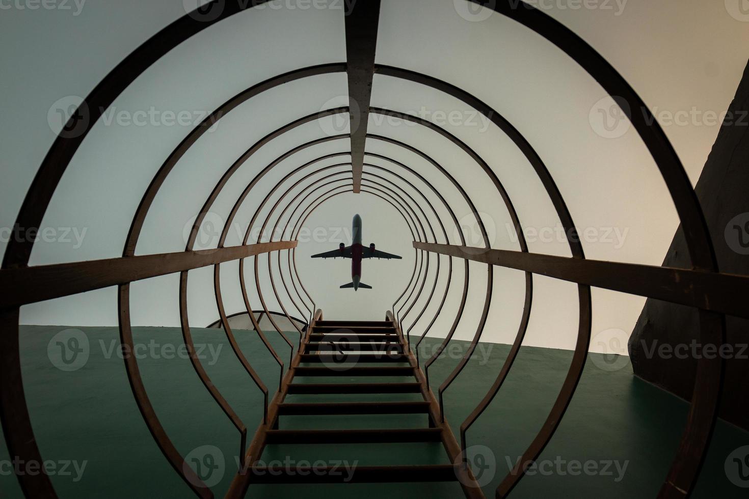 A circular steel ladder with a plane in the sky at sunset photo