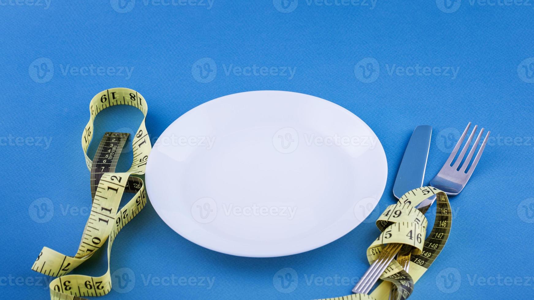 White plate on a blue background, measuring tape with a fork and knife photo