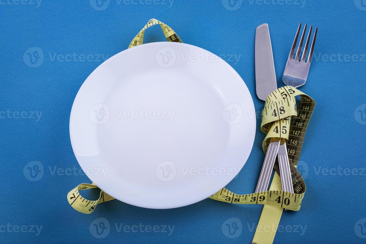White plate on a blue background, measuring tape with a fork and knife photo