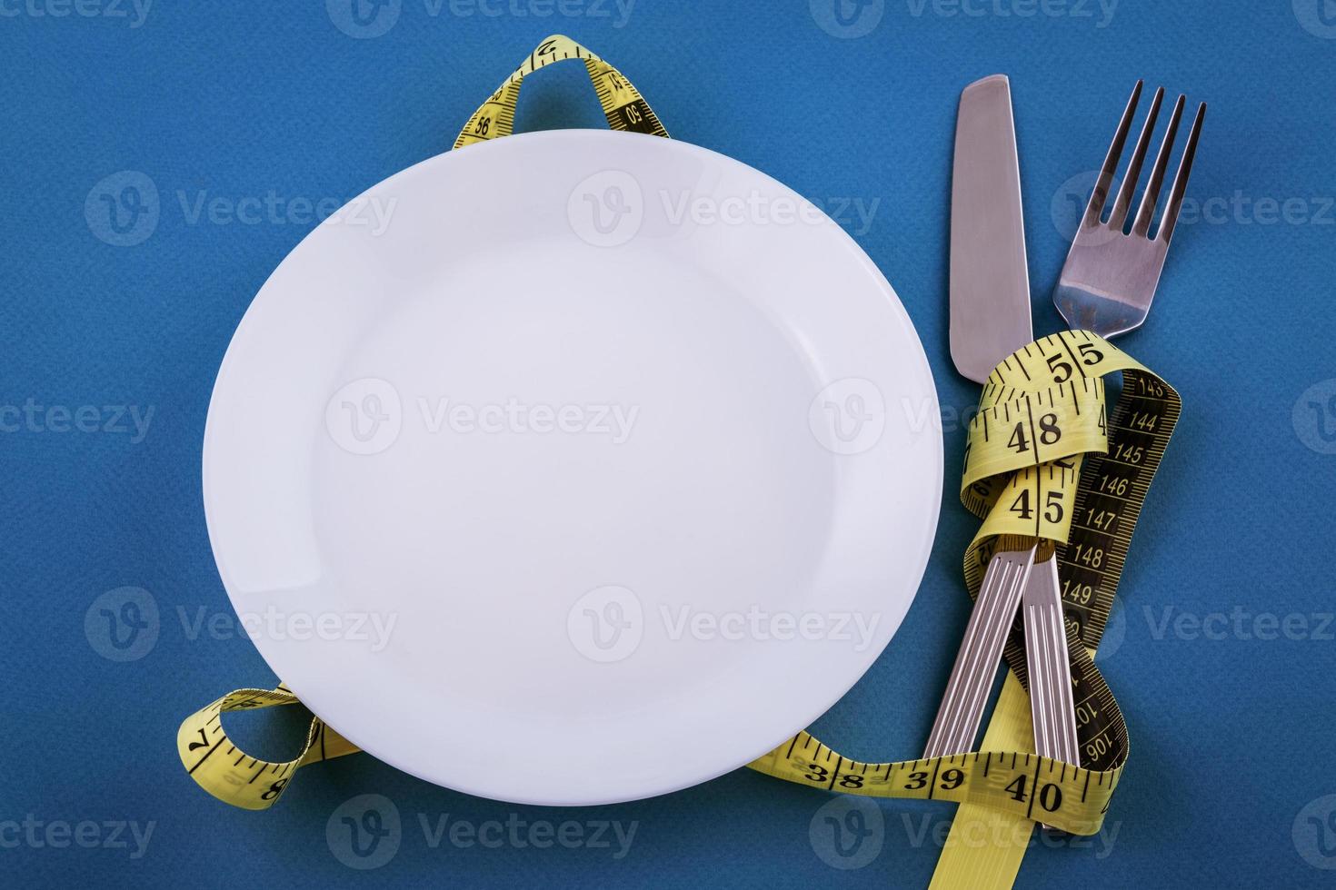 Empty white plate with devices on a blue background with measuring tape, weight loss concept photo