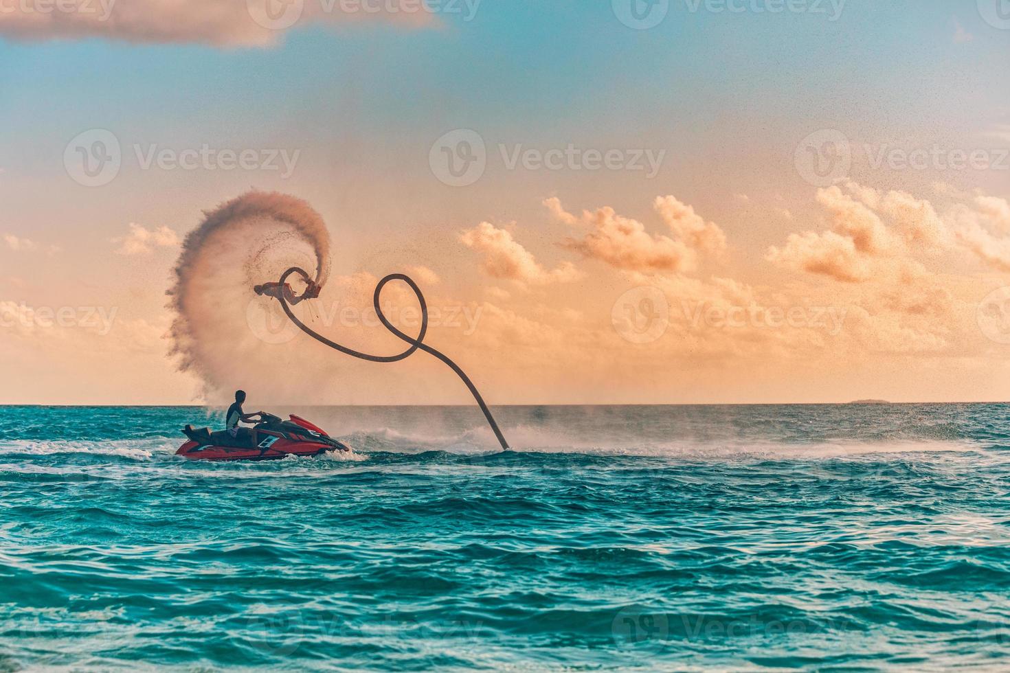 silueta de un piloto de flyboard en el mar. el jinete profesional hace trucos en la laguna azul. equipo de deportes acuáticos tropicales. vista al mar al atardecer, deporte de verano al aire libre, actividad recreativa, salpicadura increíble foto