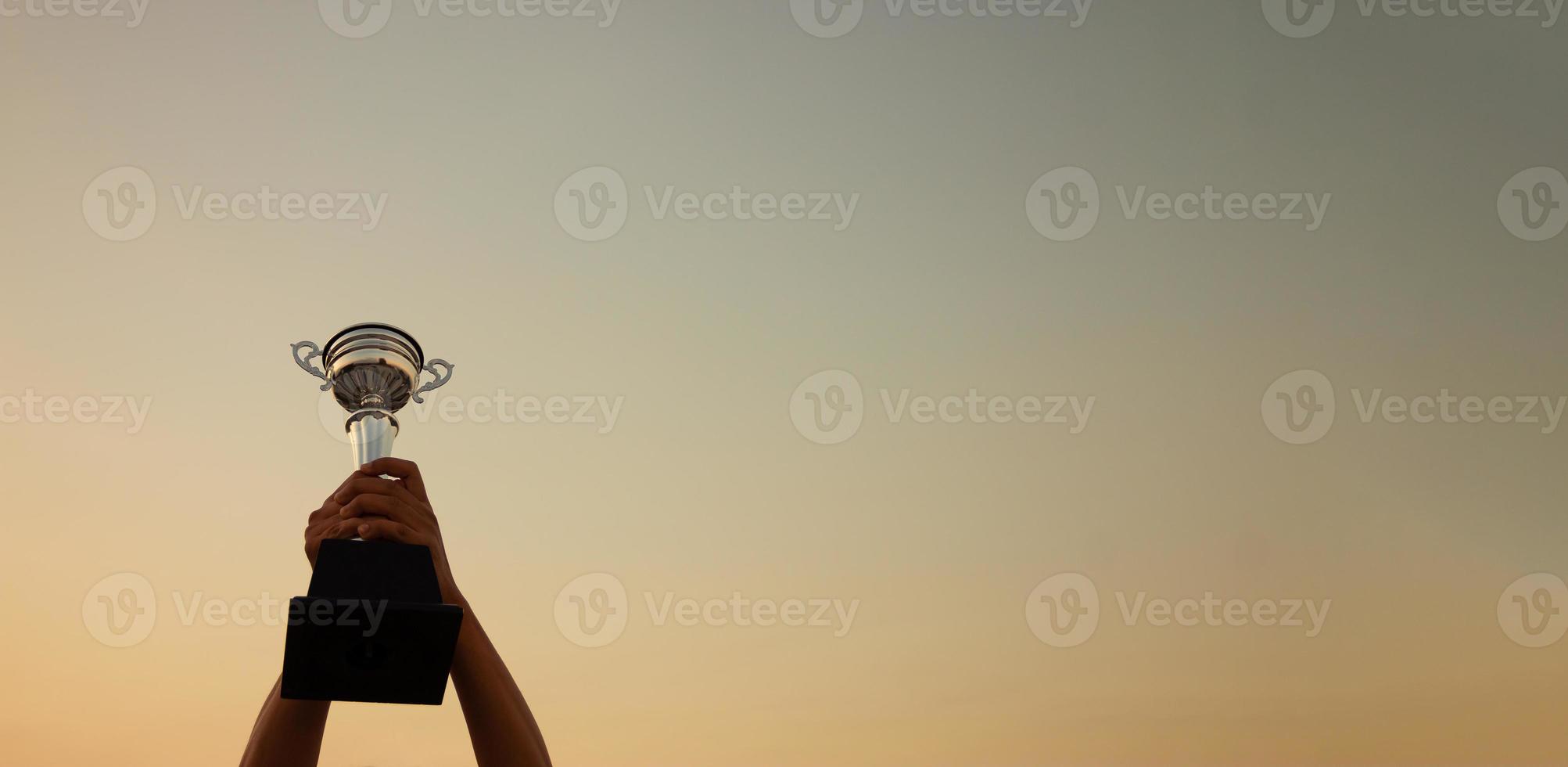 Victory concept with a hand holding a trophy on the sunset sky background, Banner design photo