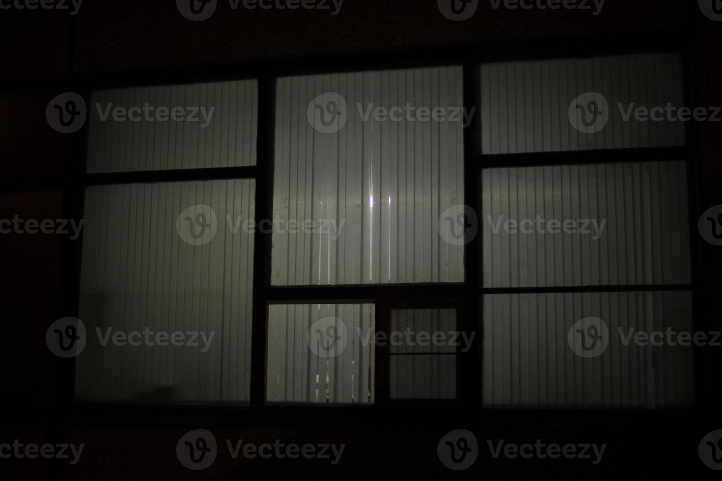 Big window at night. Window in building. Blinds cover light of lamp. photo