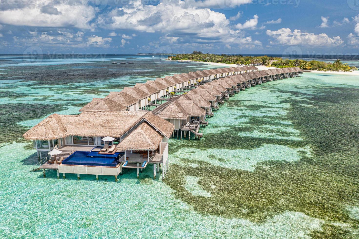 Aerial view of Maldives island, luxury water villas resort and wooden pier. Beautiful sky and ocean lagoon beach background. Summer vacation holiday and travel concept. Paradise aerial landscape pano photo