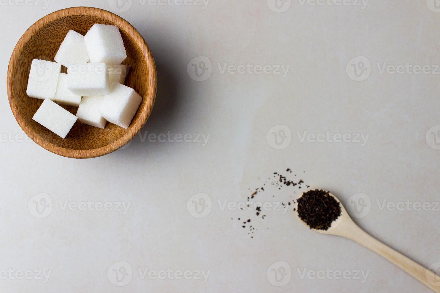 cubos de azúcar en un plato de madera y una cuchara con hojas de té en la mesa de la cocina. hacer té, pausa para el té. vista superior foto