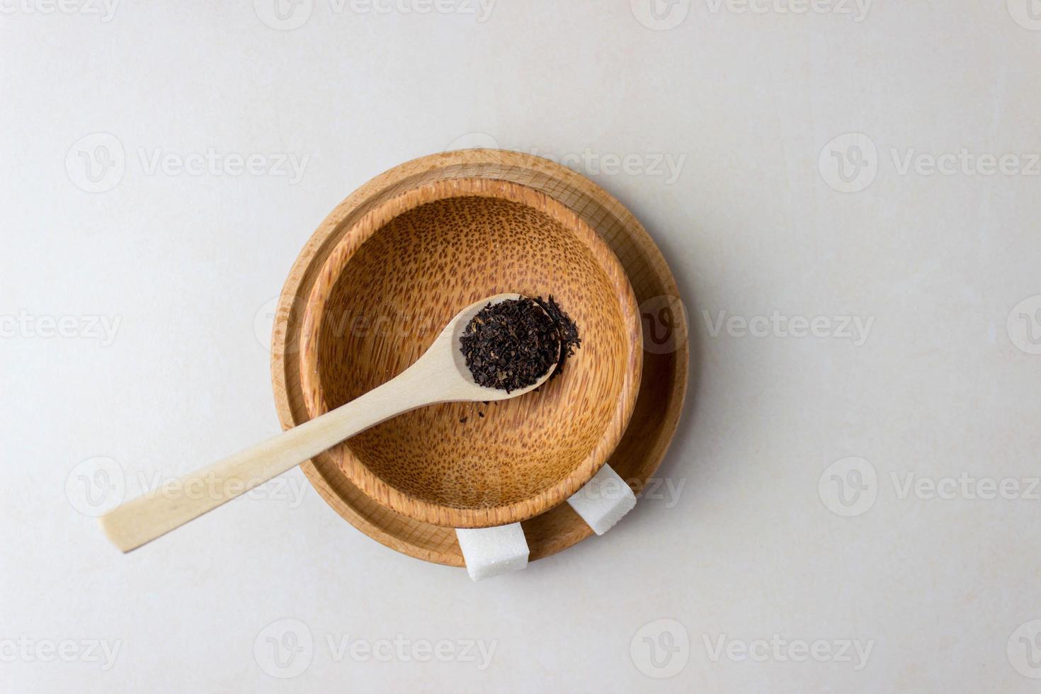 dos cubos de azúcar en un plato de madera y una cuchara con hojas de té en la mesa de la cocina. hacer té, pausa para el té. vista superior foto