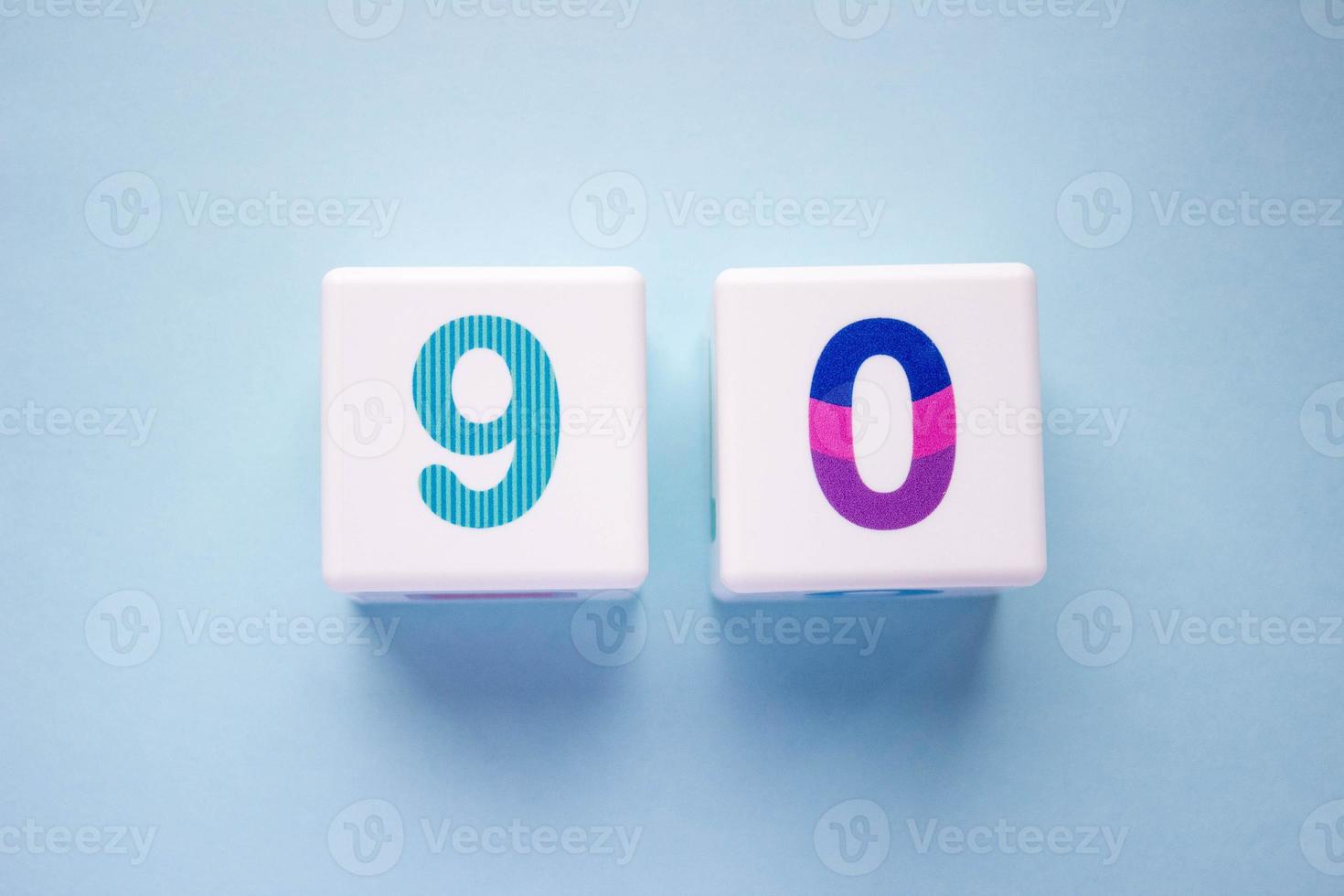 Close-up photo of a white plastic cubes with a colorful number 90 on a blue background. Object in the center of the photo