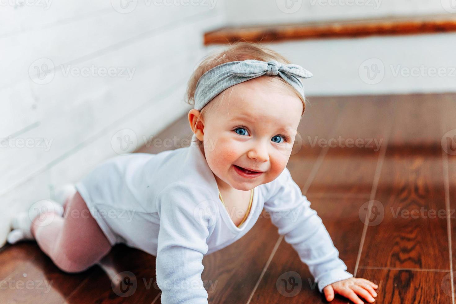 Little crawling baby girl one year old siting on floor in bright light living room near window smiling and laughing photo