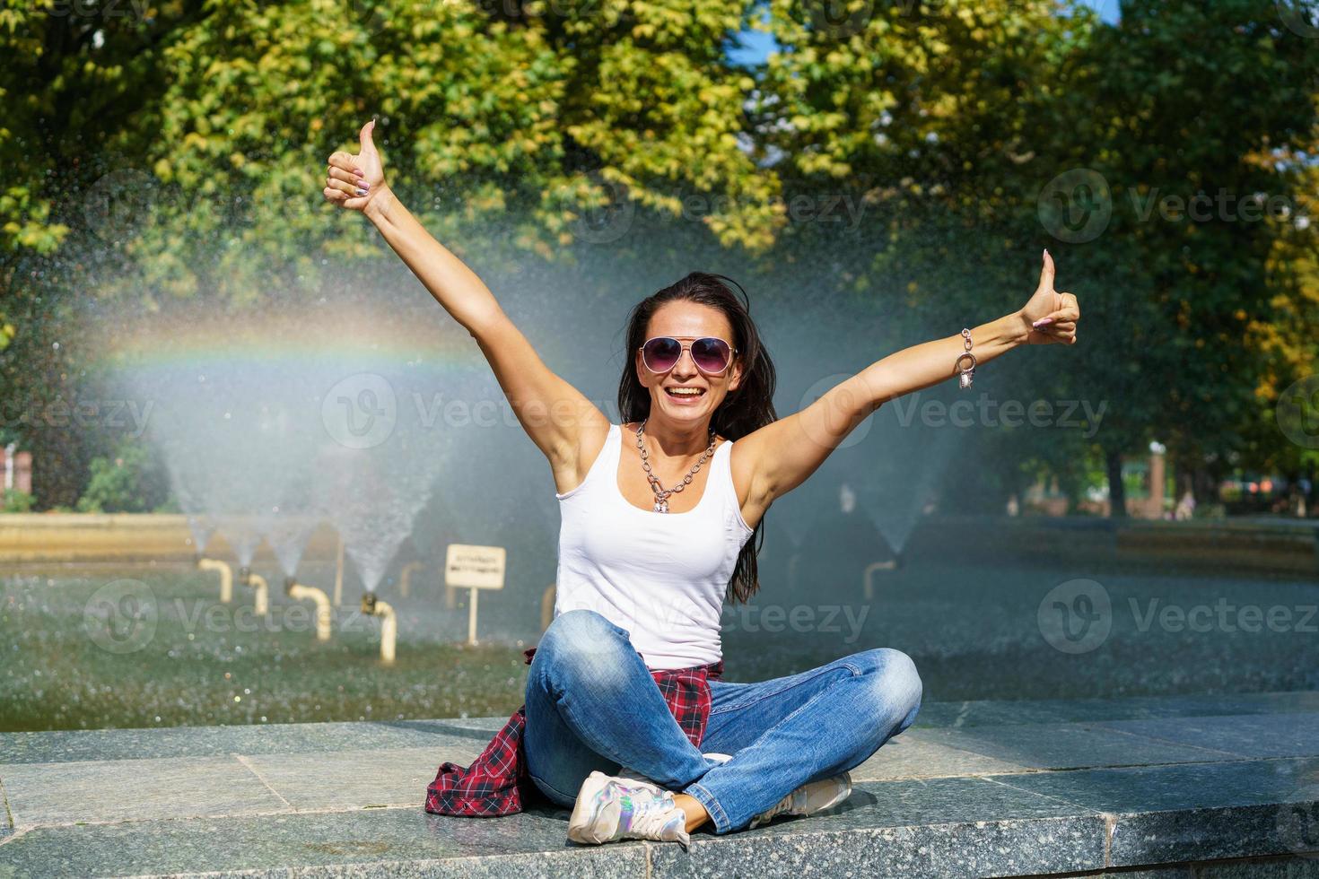 Cute caucasian woman sits by fountain in park on sunny day, enjoys the coolness photo