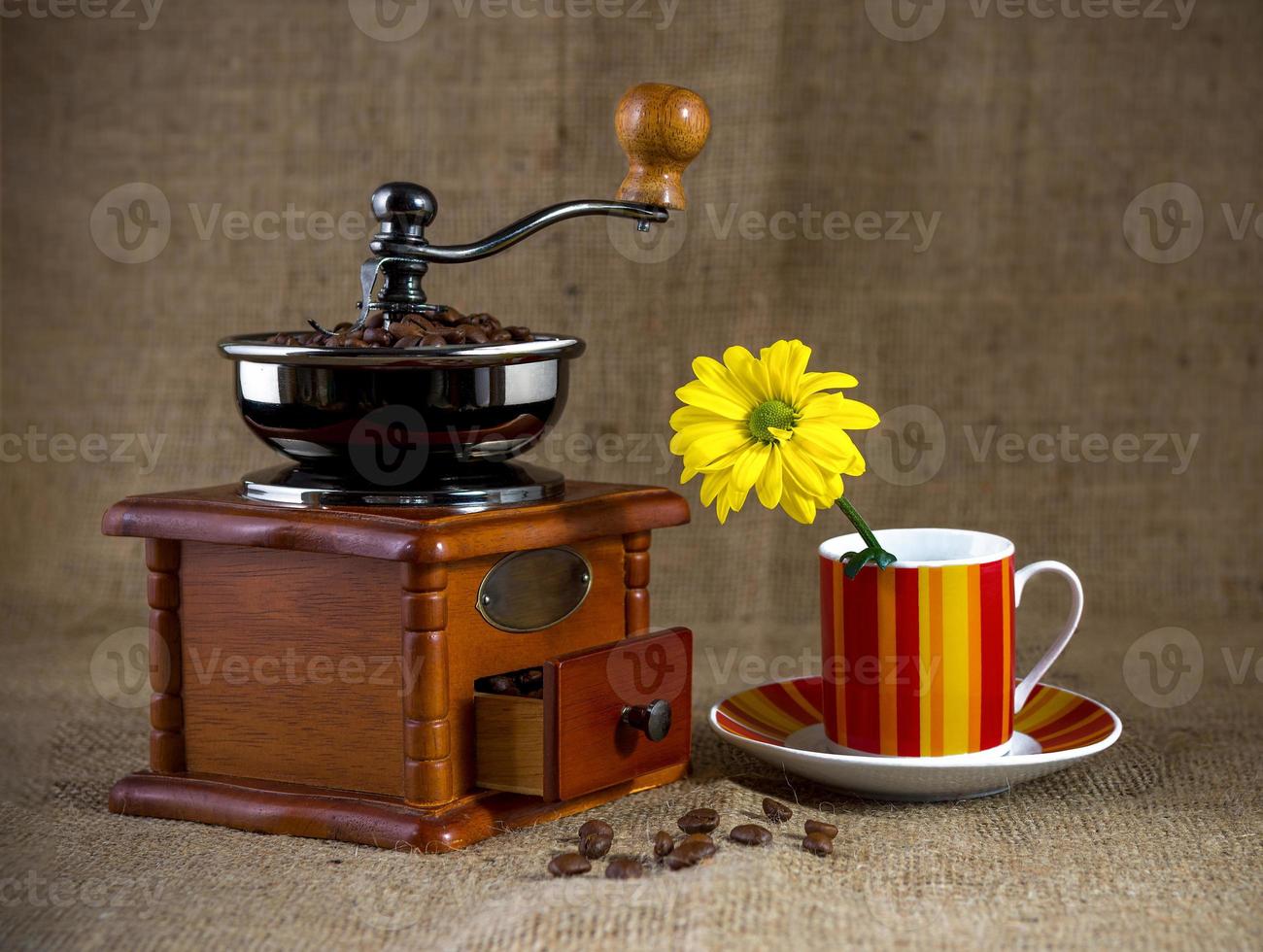 An old coffee grinder and a Cup of coffee with a yellow flower photo