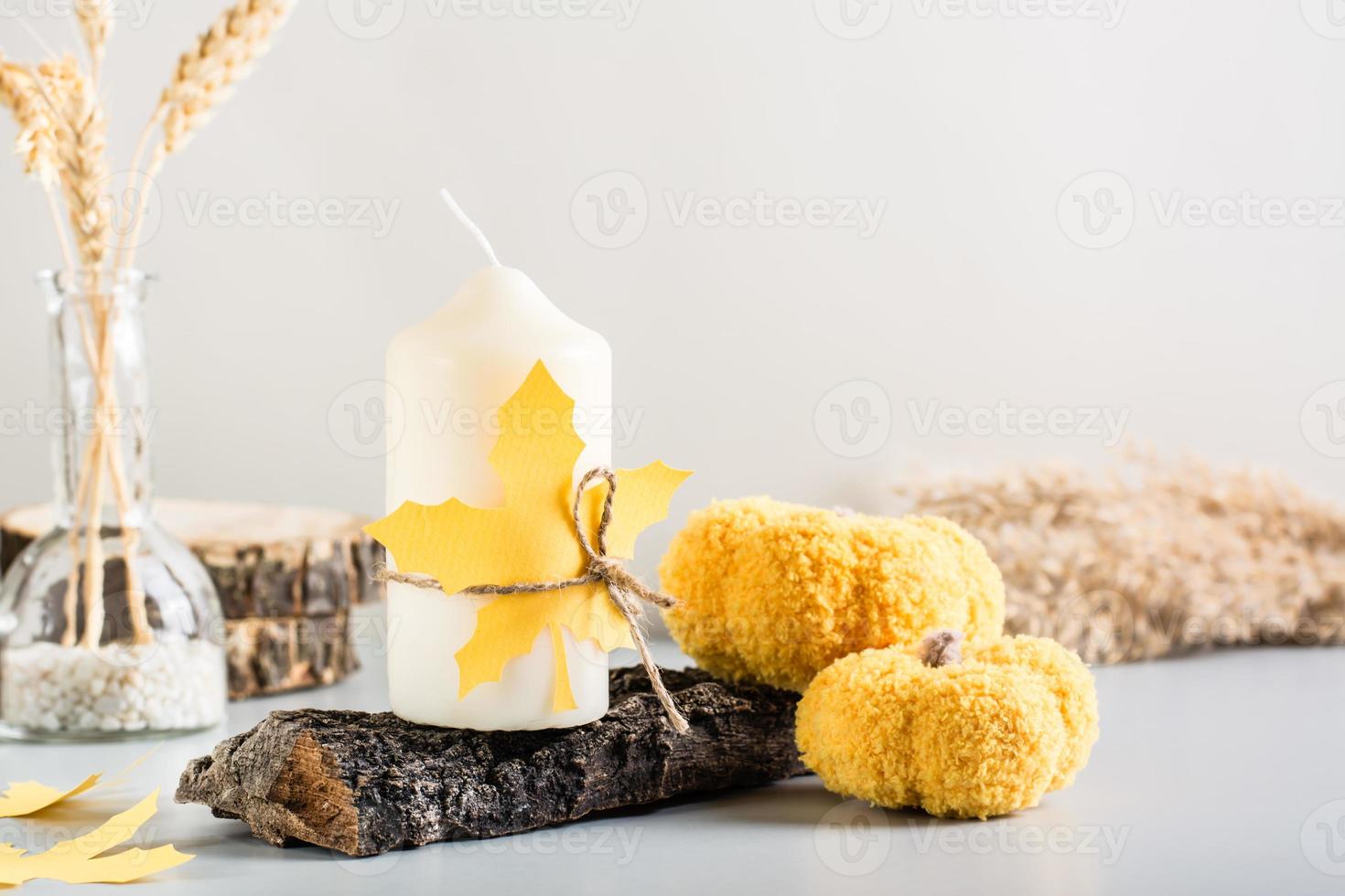 Autumn decoration. Candle on tree bark, knitted pumpkin and paper maple leaves on a light background photo