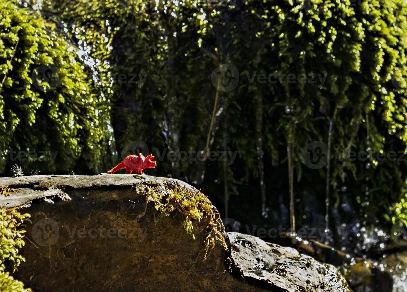 toy of red dinosaur on stone among mountain vegetation of streams. global warming photo