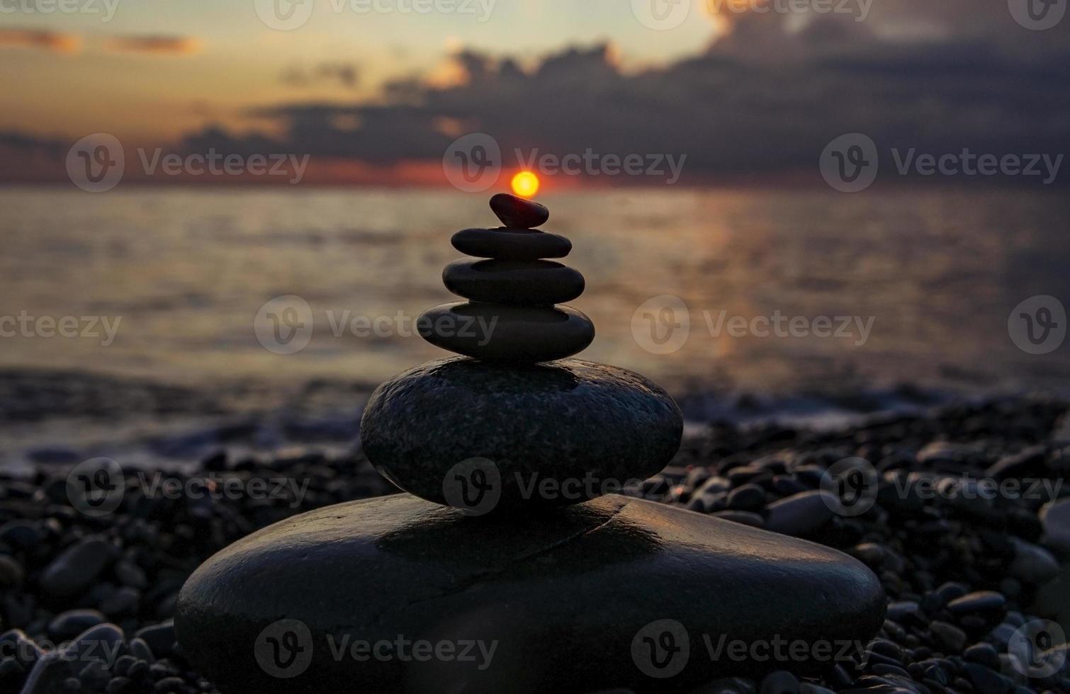 pirámide o torre de piedras de canto rodado contra el fondo del mar y el cielo del atardecer. piedras zen, concepto de meditación foto