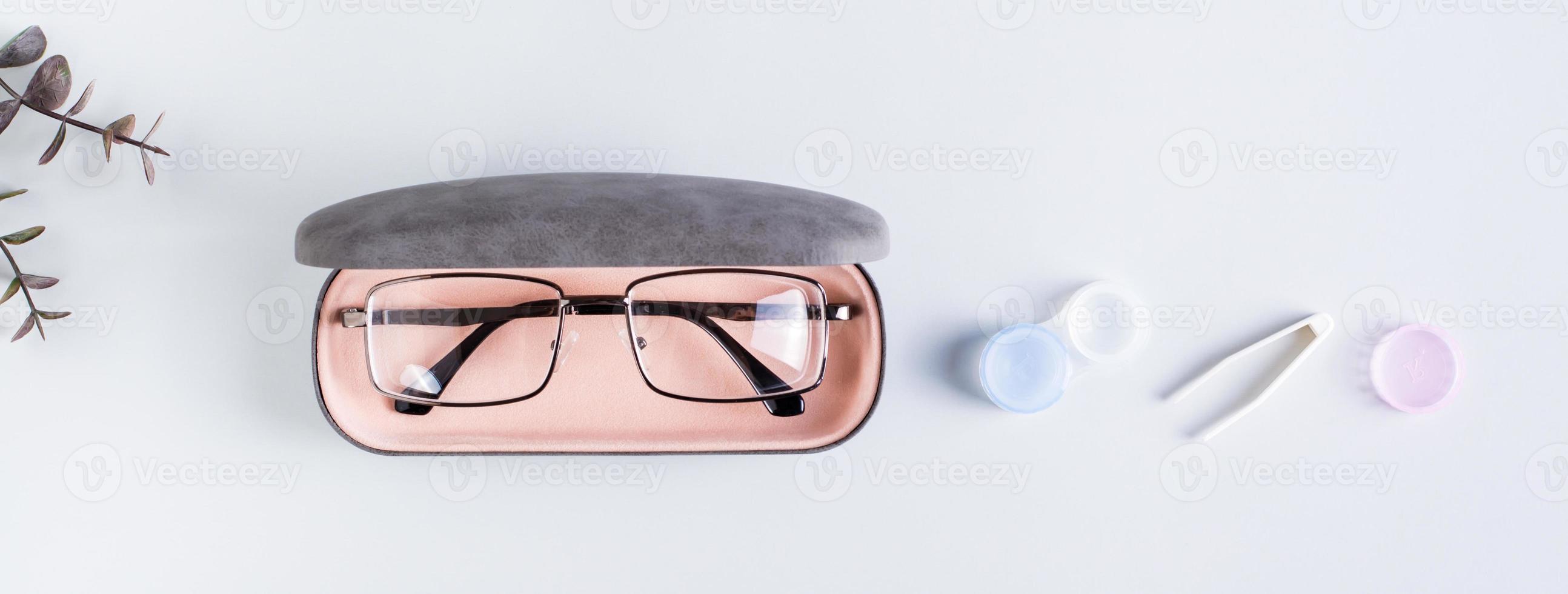 A case with glasses, an open container with contact lenses and tweezers. Top view. Web banner photo