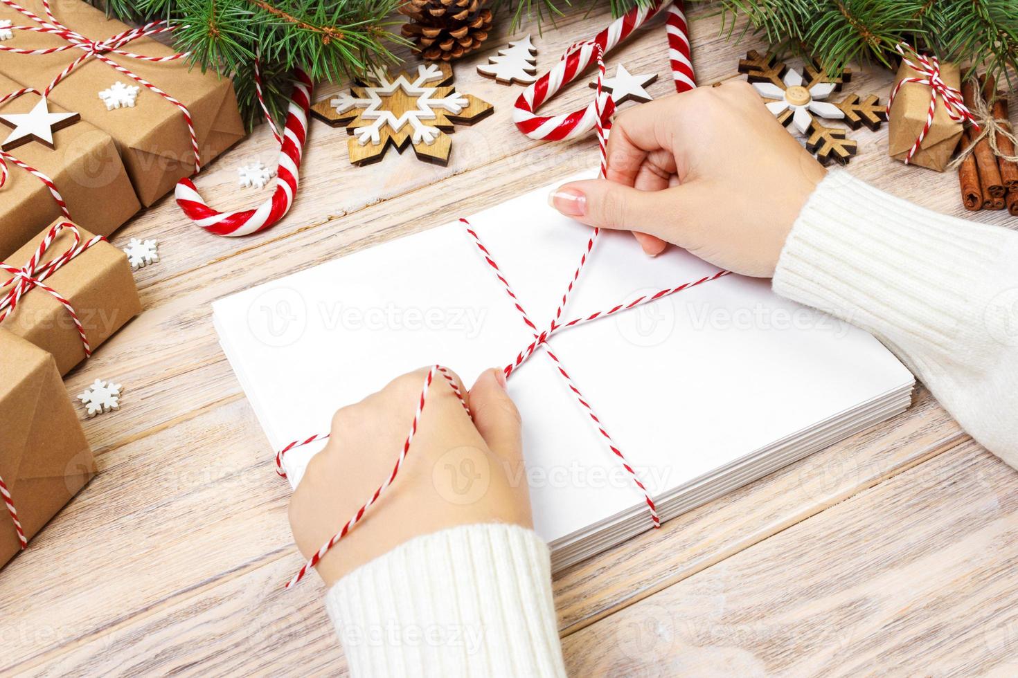 Many envelopes tied with rope. Close-up top view of famale hands with envelope. Pine cones and christmas decoration on old wooden table, desk photo