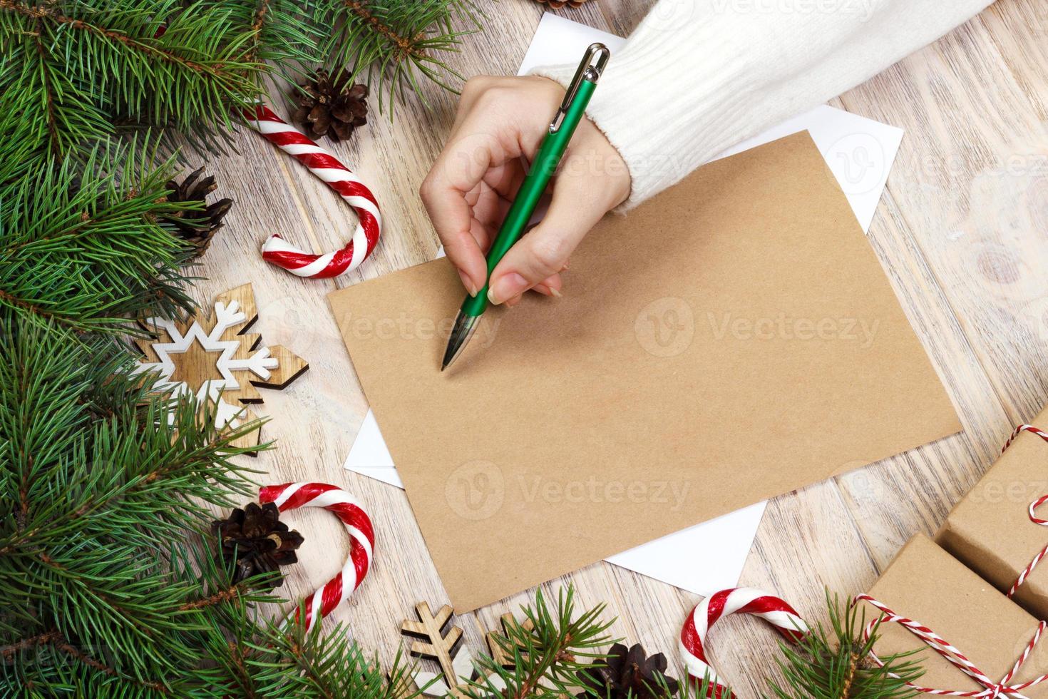 Female hands writing a letter to Santa Claus. Christmas gifts on a wooden background. View from above photo