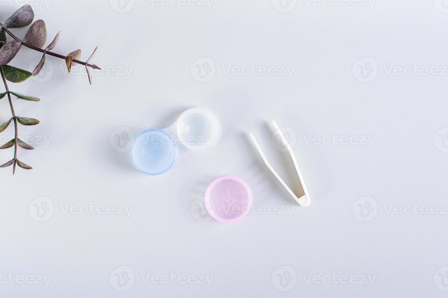 An open container with contact lenses and tweezers on a blue background. Top view. photo