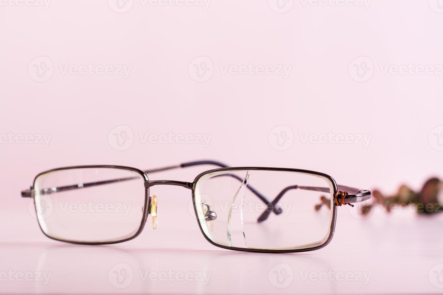 Old glasses with a broken lens and a wire attached to the shackle on a pink background photo