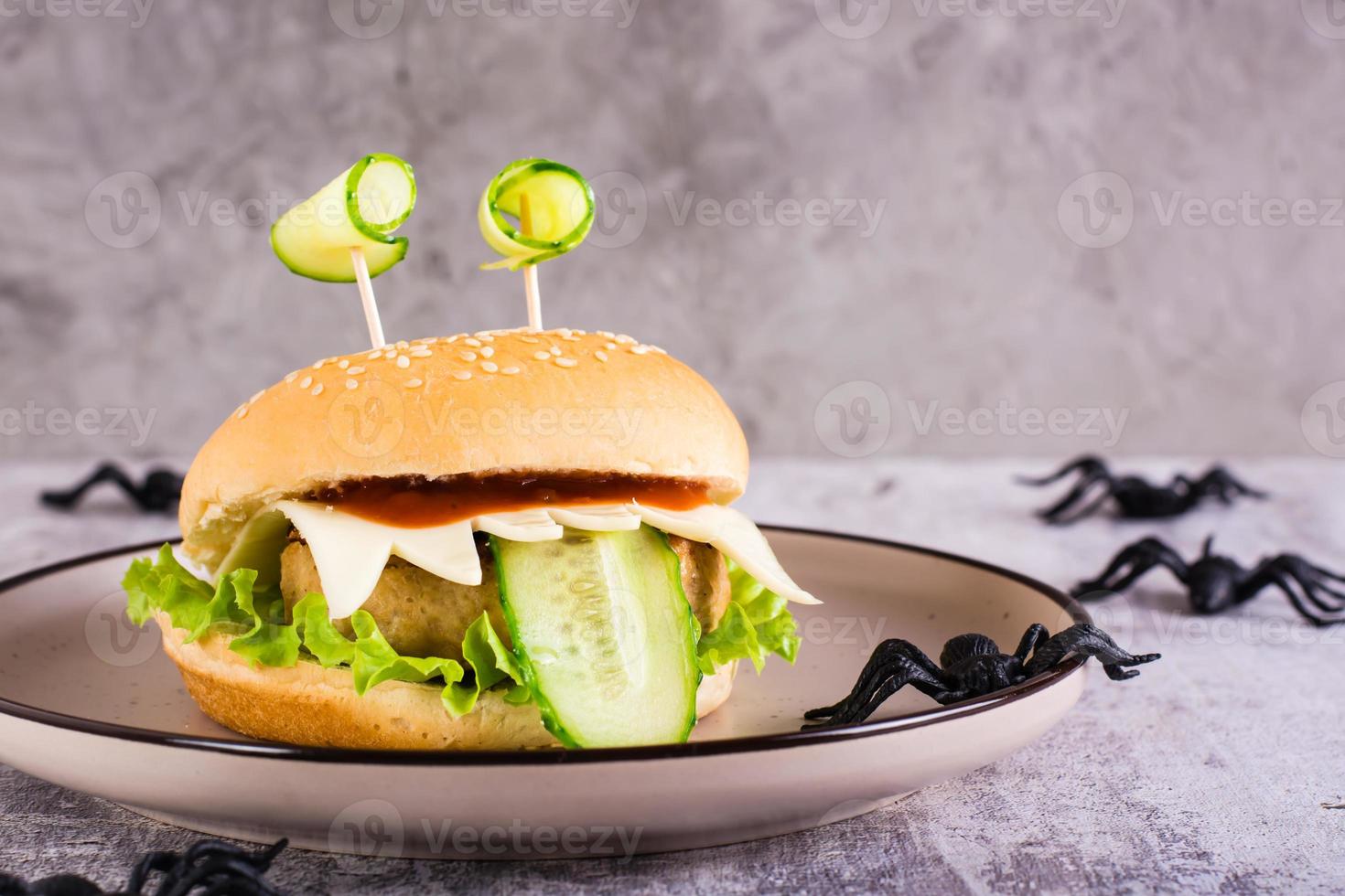 Creative burger monster with eyes and tongue for halloween menu on a plate and spiders on the table photo